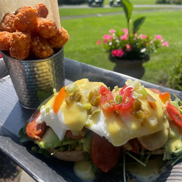 Brunch House 1850's eggs Benedict with avocado, sausage, and tater tots on an outdoor patio.
