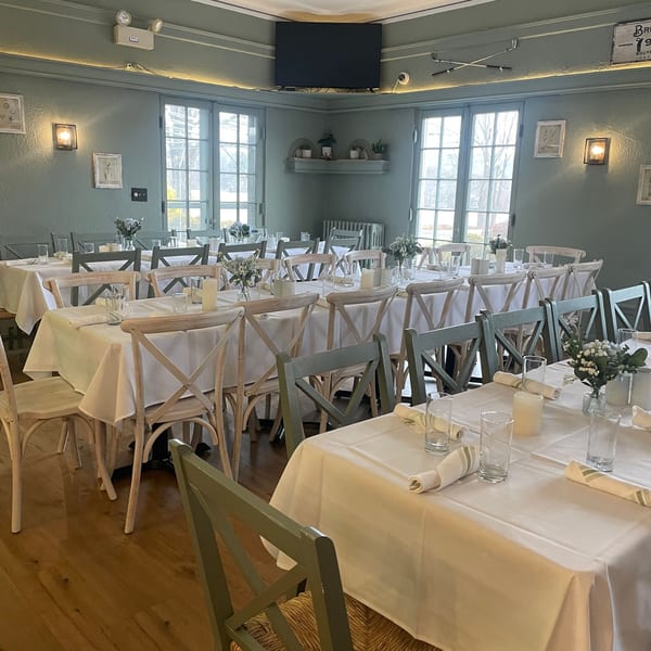 Dining room at Brunch House 1850 with set tables, light green chairs, and large windows.