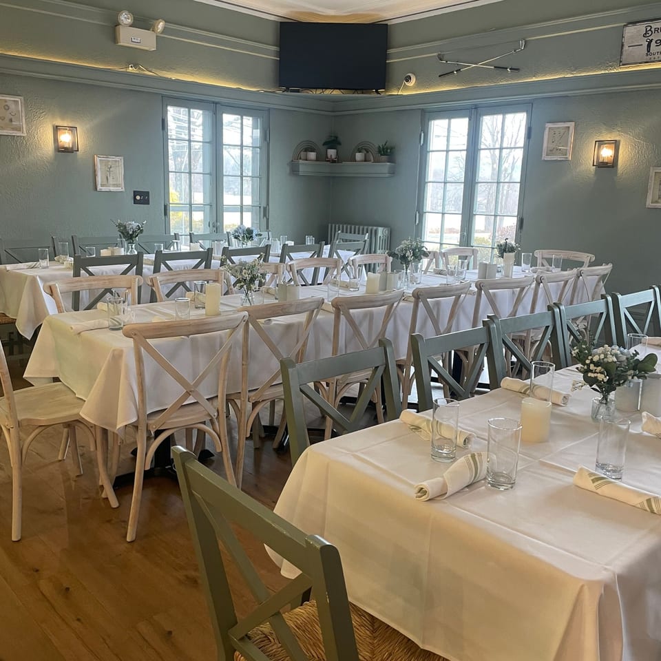 Dining room at Brunch House 1850 with set tables, light green chairs, and large windows.