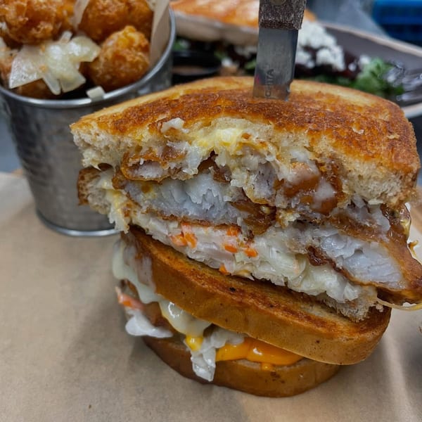 A stacked grilled cheese sandwich with fish, cheese, and coleslaw, served with tater tots.