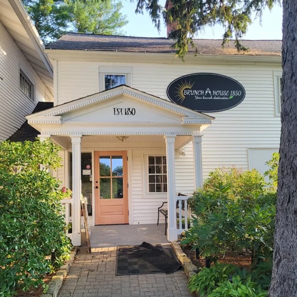The exterior of Brunch House 1850, a white building with a porch and peach-colored door.