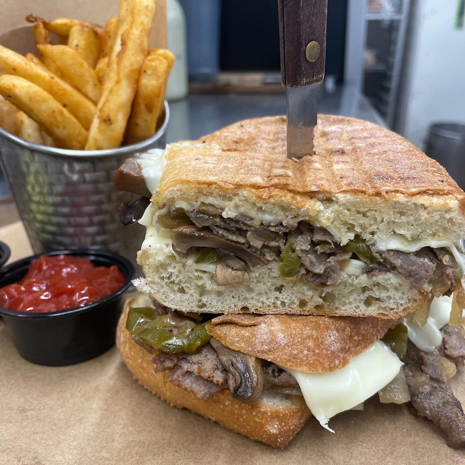 A steak and cheese sandwich with mushrooms and peppers, served with fries and ketchup.