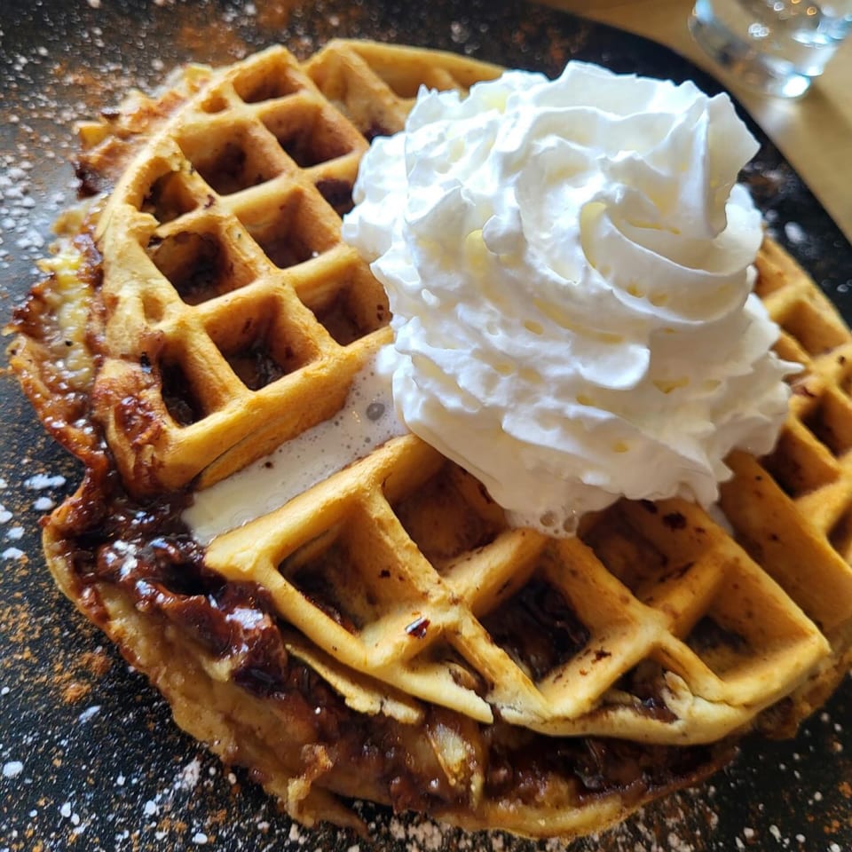 Golden waffles topped with a generous dollop of whipped cream and a dark, gooey sauce.