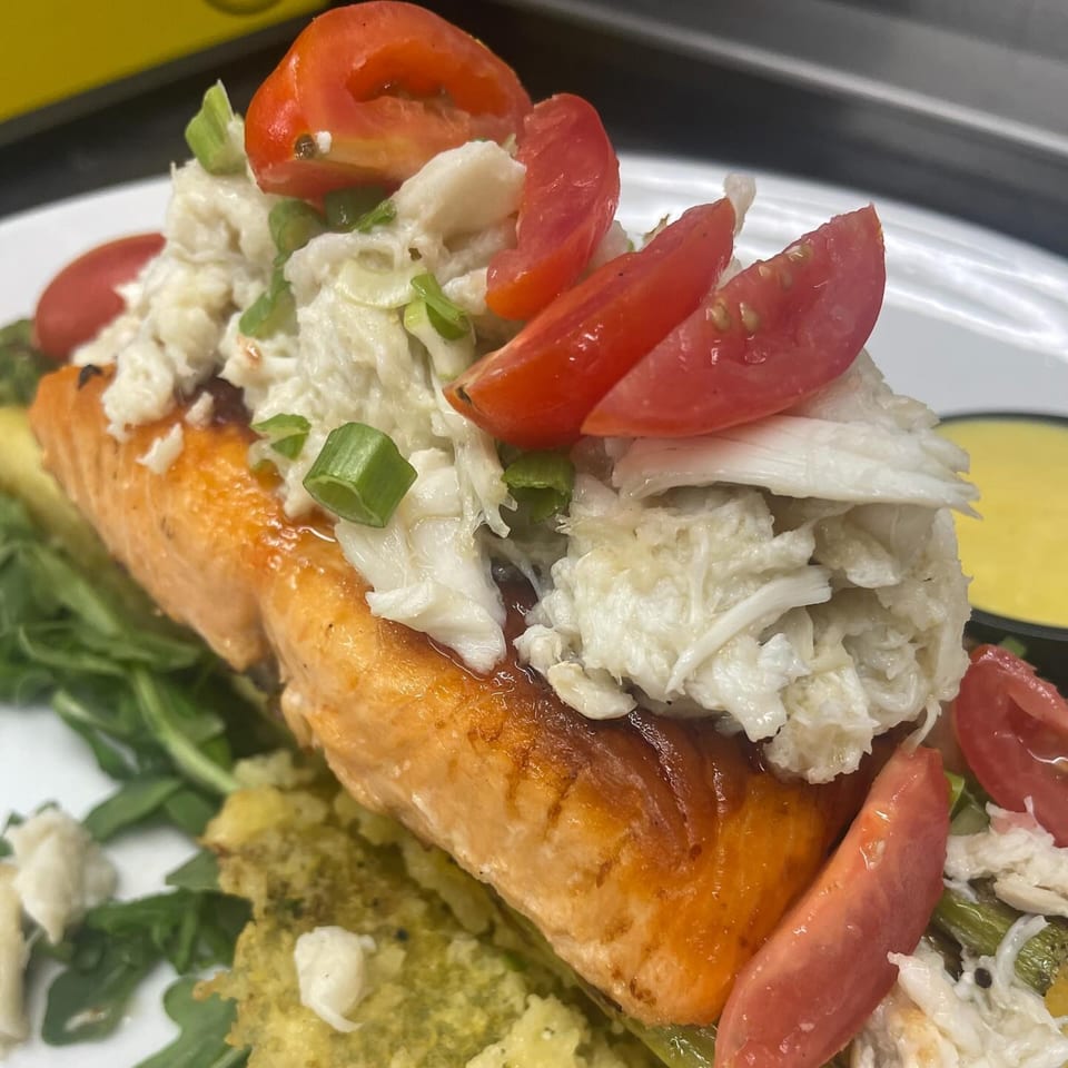 Salmon fillet topped with crab meat, sliced tomatoes, and green onions, served with greens.