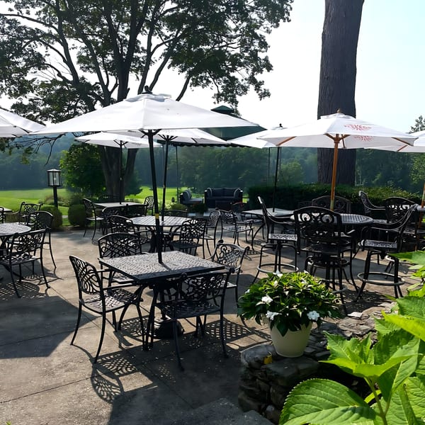 Outdoor patio at Brunch House 1850 with black wrought iron tables and chairs under white umbrellas.