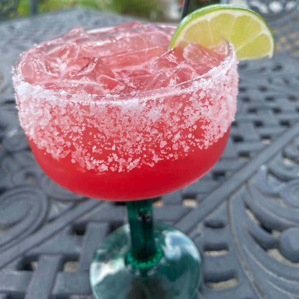 A vibrant red margarita with a salted rim and lime wedge, on a dark outdoor table.