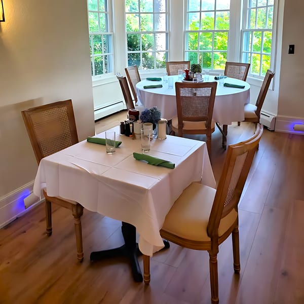 Dining room at Brunch House 1850 with set tables, white tablecloths, and large windows overlooking greenery.