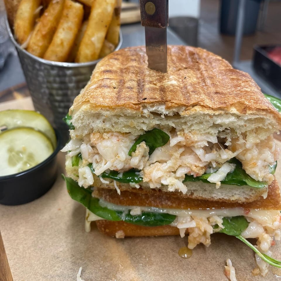 A lobster panini with spinach and cheese, served with a side of fries and pickles.