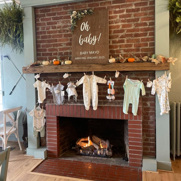 A fireplace with baby clothes hanging on a line and a sign announcing "Oh baby! Baby Mayo arriving January 2025".