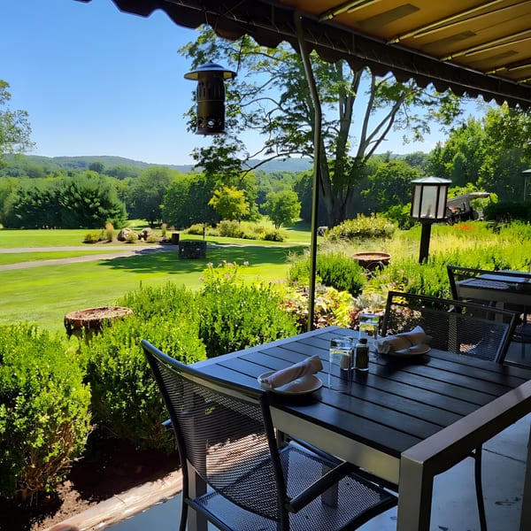 Outdoor dining table at Brunch House 1850 with a scenic view of a golf course and green hills.